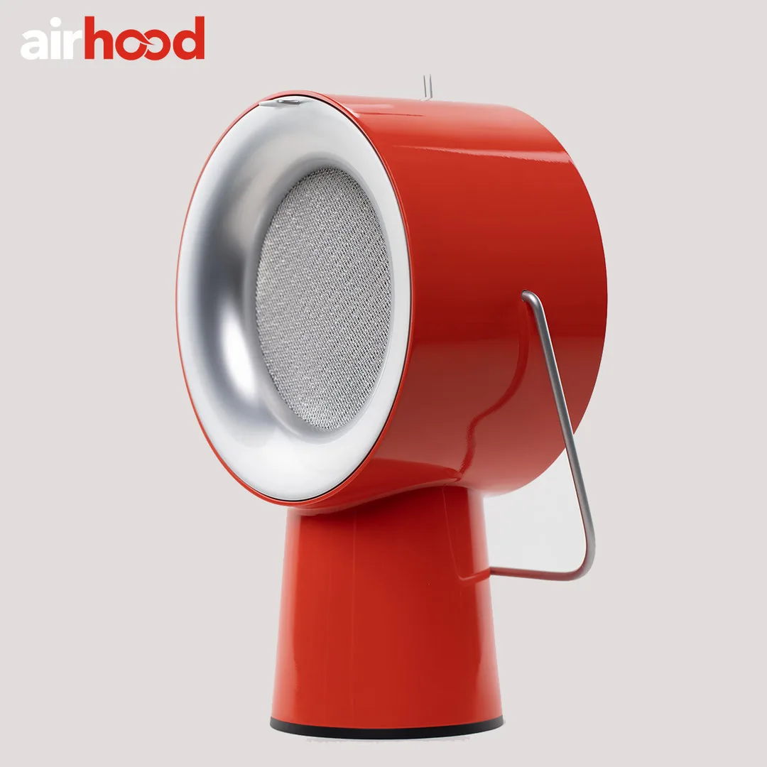 AirHood ad image: the red AirHood in three-quarter view on a plain pale grey backdrop, its silver filter face and wire handle catching the light, under the airhood wordmark