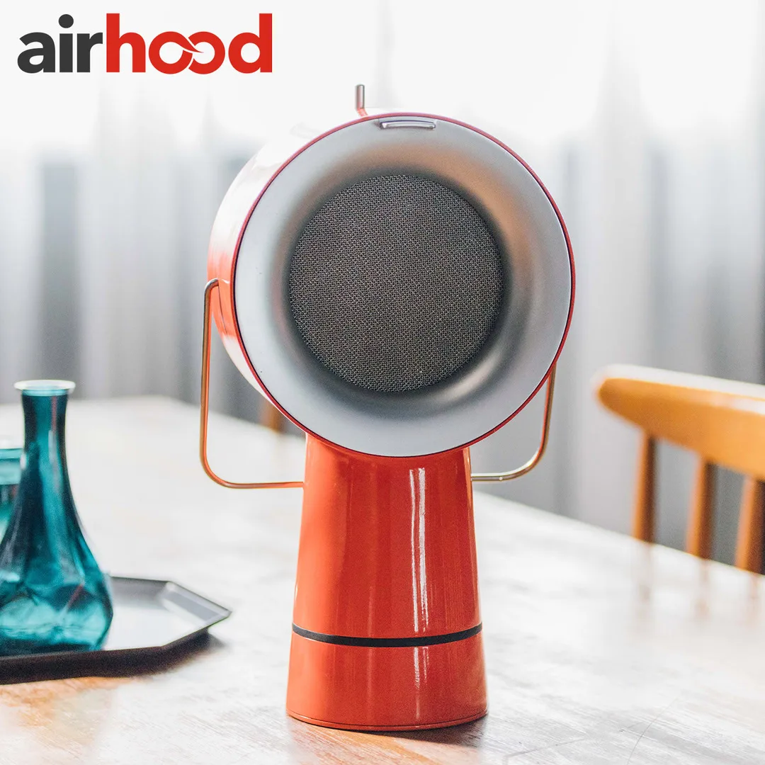 AirHood ad image: the red AirHood on a wooden dining table beside a teal glass carafe on a tray, a window and a wooden chair soft behind it, under the airhood wordmark