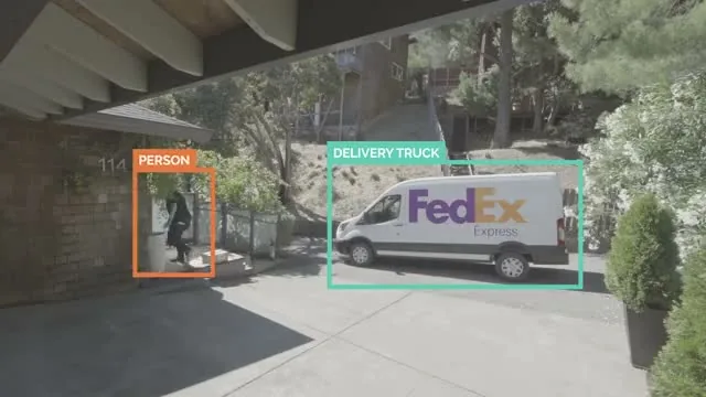 Security-camera view of a driveway with labeled detection boxes: PERSON around someone at the front door, DELIVERY TRUCK around a FedEx van