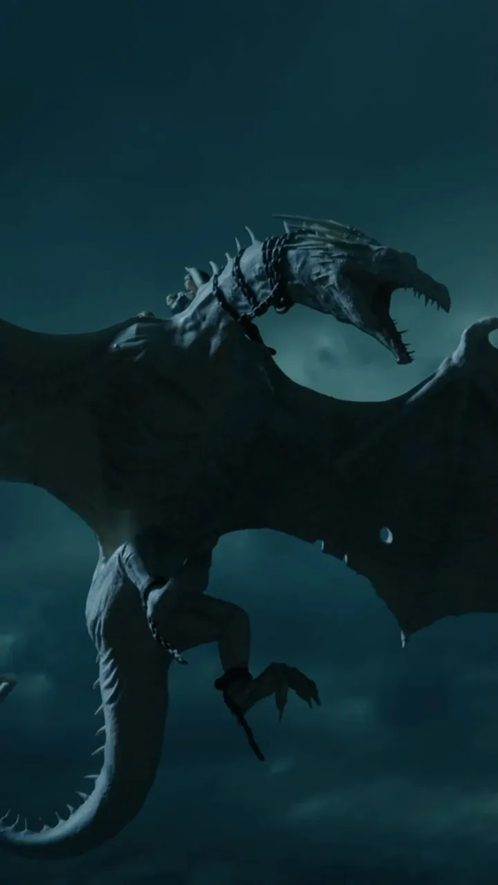 Video still: a pale, chained dragon flies open-jawed through a stormy night sky