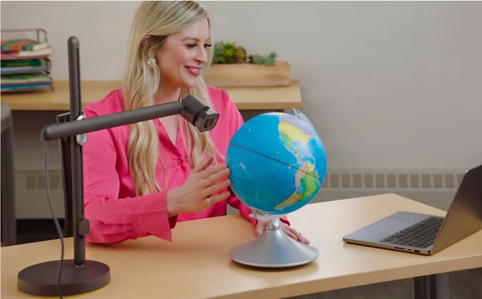 An educator points the Reach camera head at a globe beside her laptop.
