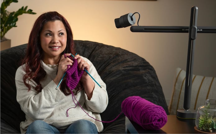 A creator knits on a beanbag while Reach films her hands from above.
