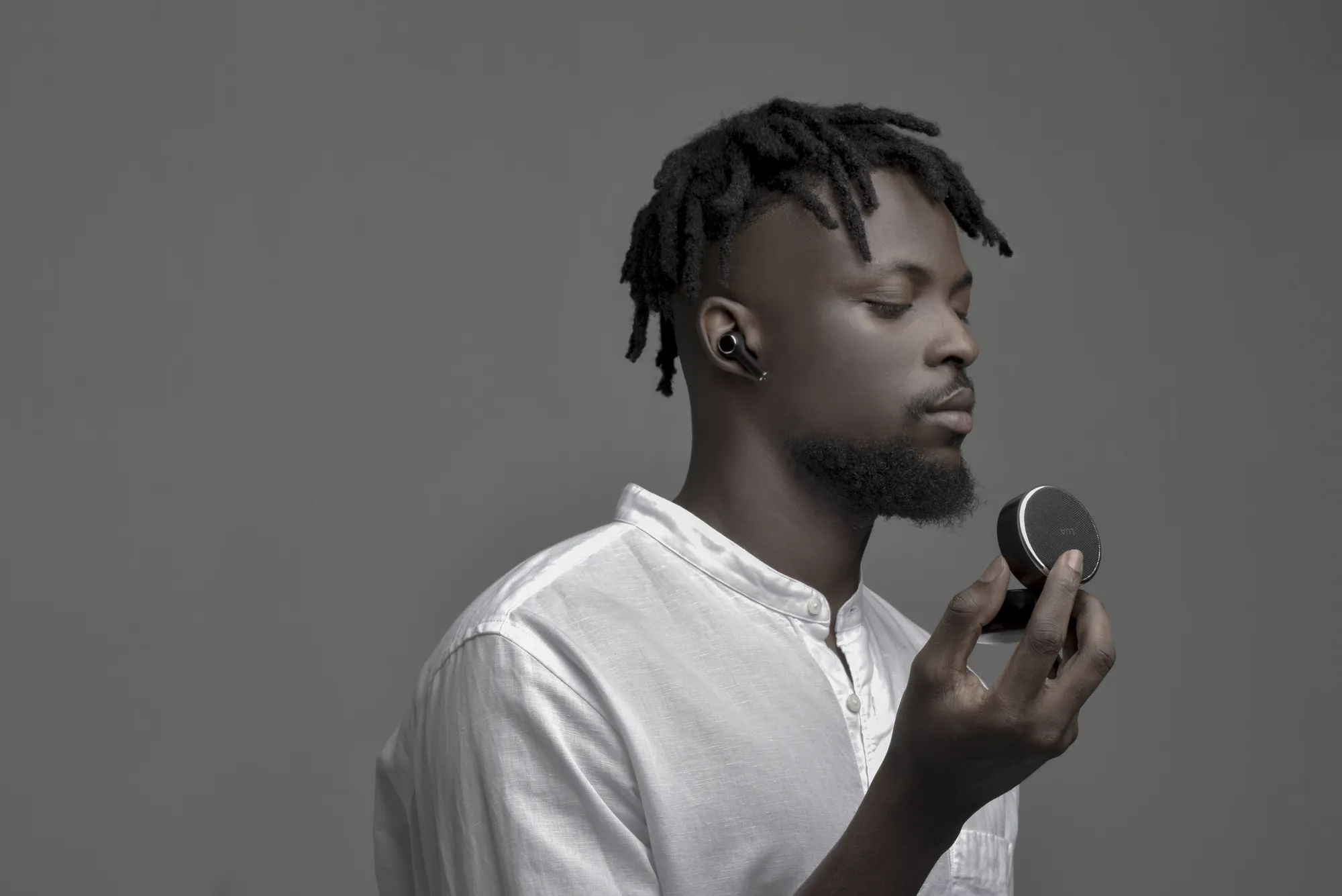 A man with a LUA earphone in his ear holds the speaker charging case up to his chin, listening with his eyes closed.