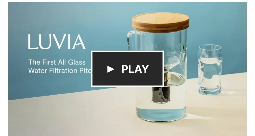 Campaign video still: the all-glass Luvia pitcher and a filled glass on a blue backdrop — LUVIA, The First All Glass Water Filtration Pitcher — with a play button.
