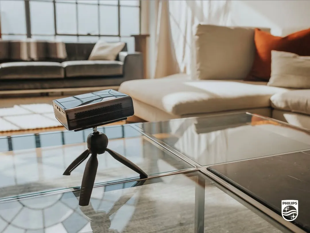 The PicoPix Max on a mini tripod on a glass coffee table in a sunlit living room