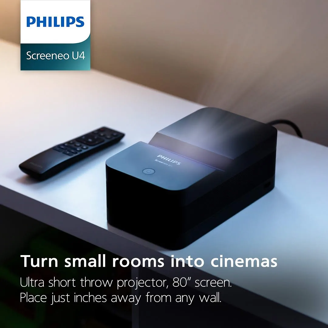 Screeneo U4 ad: the projector on a white desk beside its remote, glowing where it throws light up the wall, under a Philips Screeneo U4 badge, with the lines Turn small rooms into cinemas, Ultra short throw projector, 80” screen, Place just inches away from any wall