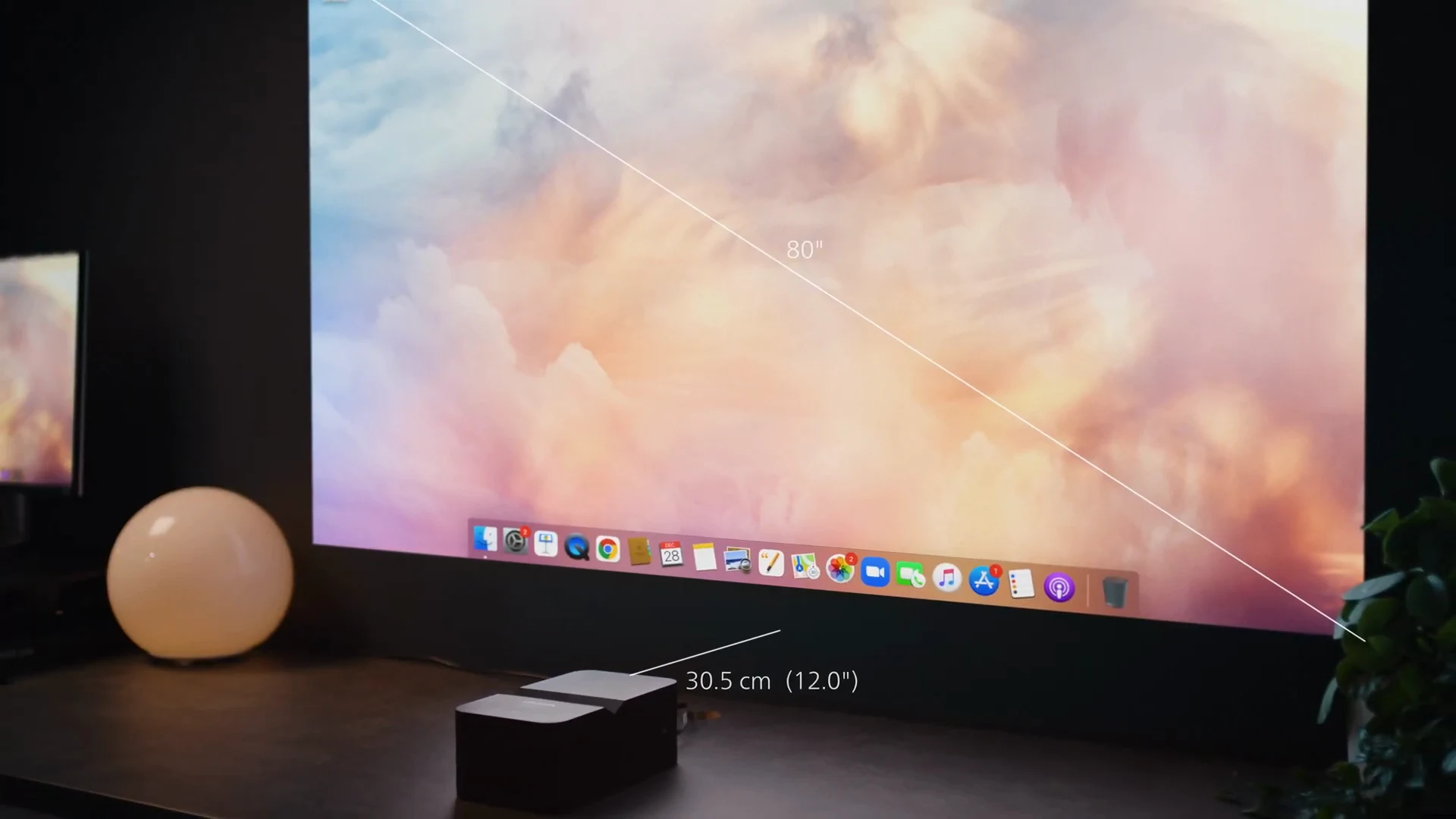 Still from the campaign film: the Screeneo U4 on a desk against the wall, an 80-inch sunset filling the wall above it, with the film's own measurements marking the 80-inch diagonal and the 30.5 cm (12 in) gap to the wall.