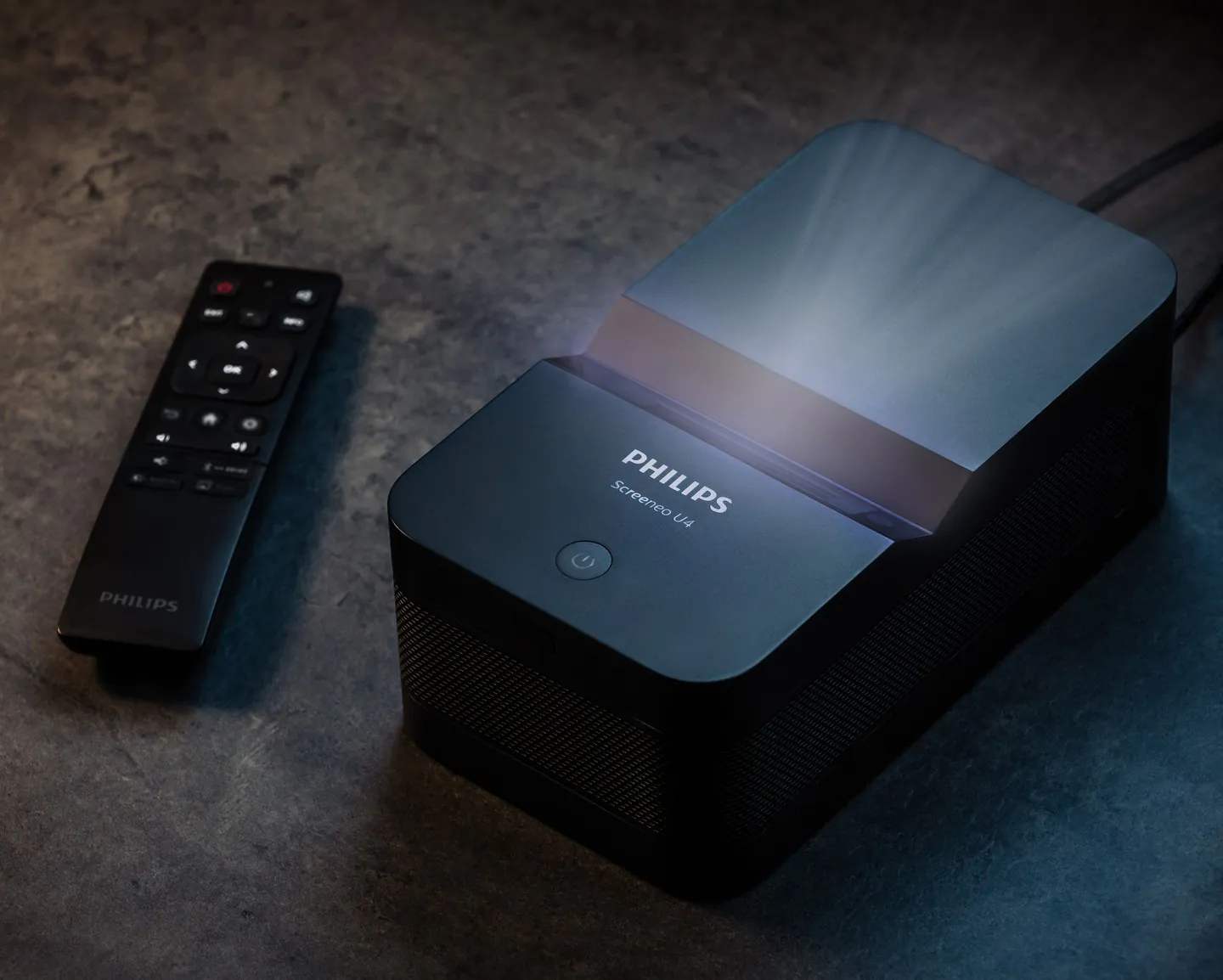 The black Philips Screeneo U4 on a stone surface, light rising from its top, its remote beside it