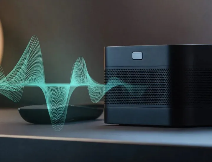 The black Screeneo U4 on a shelf beside its remote, a teal sound-wave graphic flowing from its speaker grille