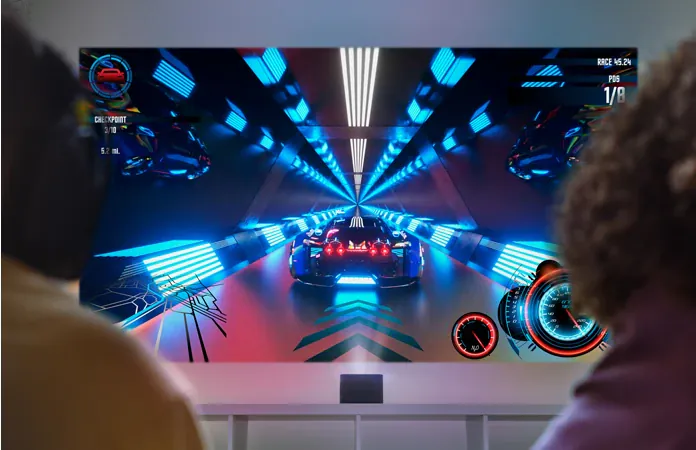 Two players, seen from behind, face a racing game projected large on the wall from the U4 on a low console.