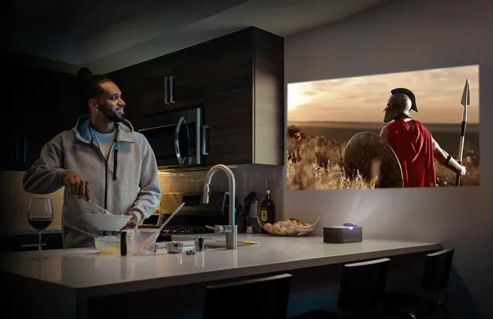 A man cooking at a kitchen counter turns toward a spear-carrying warrior projected on the wall beside him, the U4 on the counter below the picture.