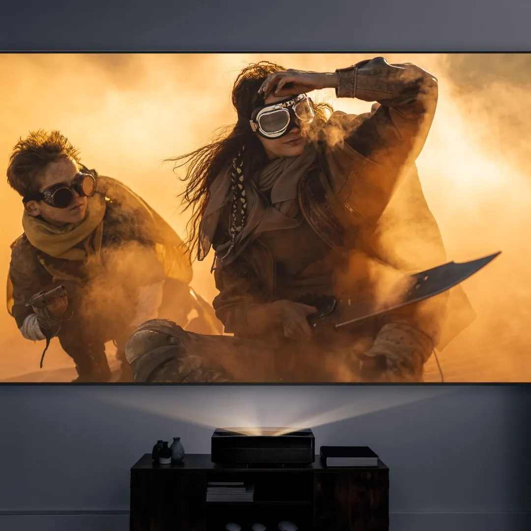 A Screeneo U5 on a low cabinet projects a wall-size film still of two goggled figures crouching in orange desert haze