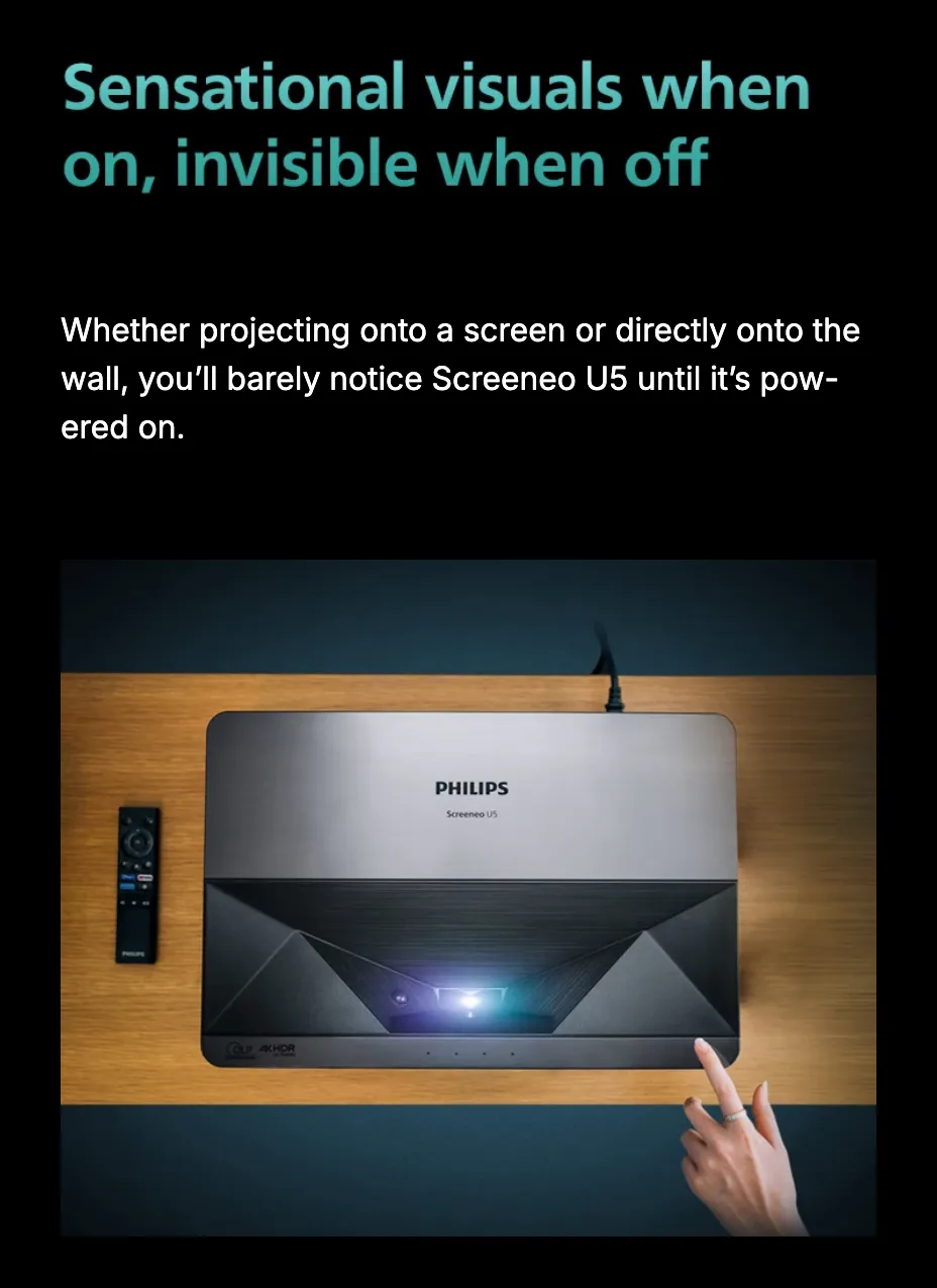 Sensational visuals when on, invisible when off. Whether projecting onto a screen or directly onto the wall, you'll barely notice Screeneo U5 until it's powered on — seen from above, the projector lies on a wood plank against a teal ground, a remote beside it and a hand reaching in from the right.
